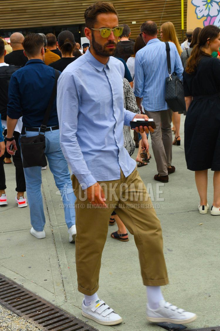 A spring/summer men's coordinate outfit with solid color sunglasses, solid color blue shirt, solid color beige chinos, solid color socks, and white low-cut Puma sneakers.