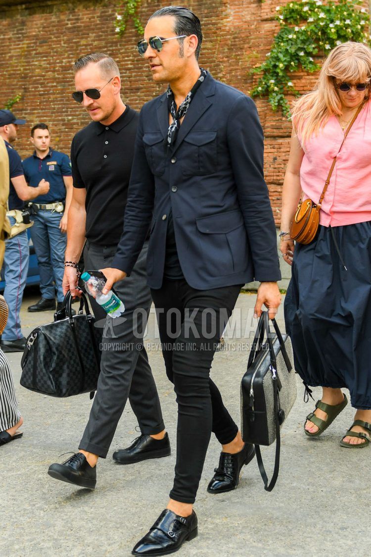 Spring/Summer/Fall men's coordinate outfit with plain silver sunglasses, black other scarf, plain navy tailored jacket, plain black t-shirt, plain black denim/jeans, black monk shoes leather shoes, plain black briefcase/handbag.