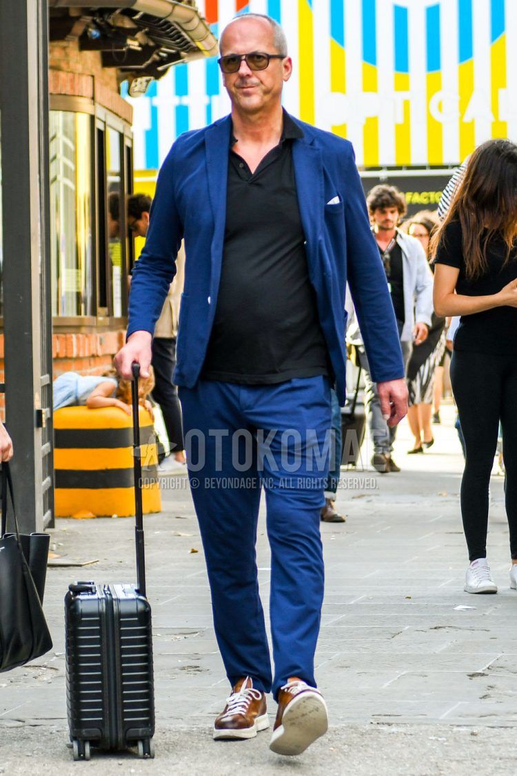 A summer-spring-fall men's coordinate outfit with plain sunglasses, a plain black polo shirt, brown low-cut sneakers, and a plain blue suit.