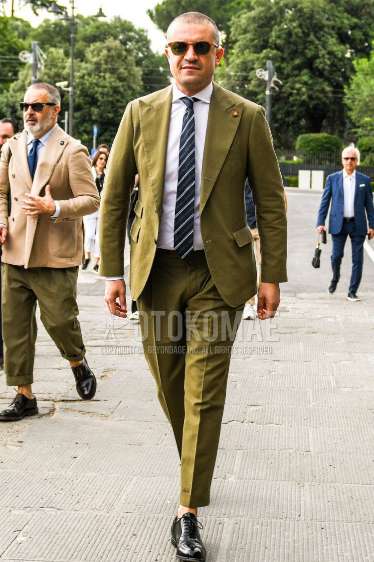 Spring, summer and fall men's coordinate outfit with brown tortoiseshell sunglasses, plain white shirt, black straight tip leather shoes, plain olive green suit and navy/white striped tie.