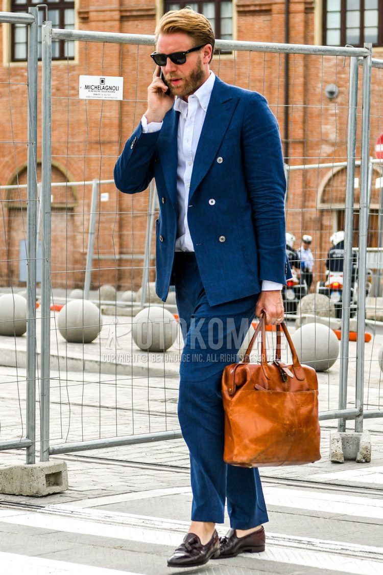 A men's spring/summer/fall outfit with plain black sunglasses, plain white shirt, brown tassel loafer leather shoes, plain brown briefcase/handbag, and plain navy suit.