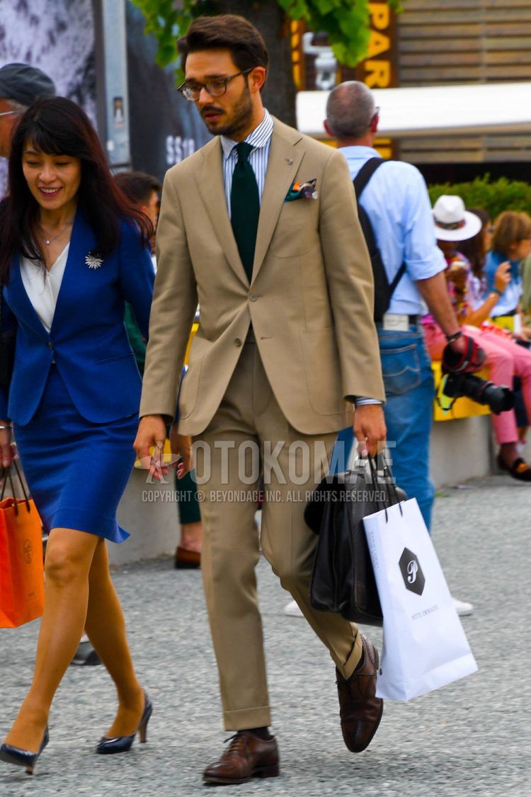 Men's spring/summer/fall outfit with plain glasses, white/light blue striped shirt, brown straight tip leather shoes, plain brown briefcase/handbag, plain beige suit, and plain navy tie.