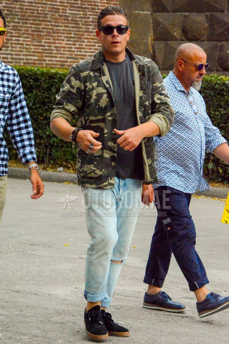Spring/Summer/Fall men's coordinate outfit with solid color sunglasses, olive green camouflage shirt jacket, solid color black t-shirt, solid color light blue denim/jeans, and black low-cut sneakers.