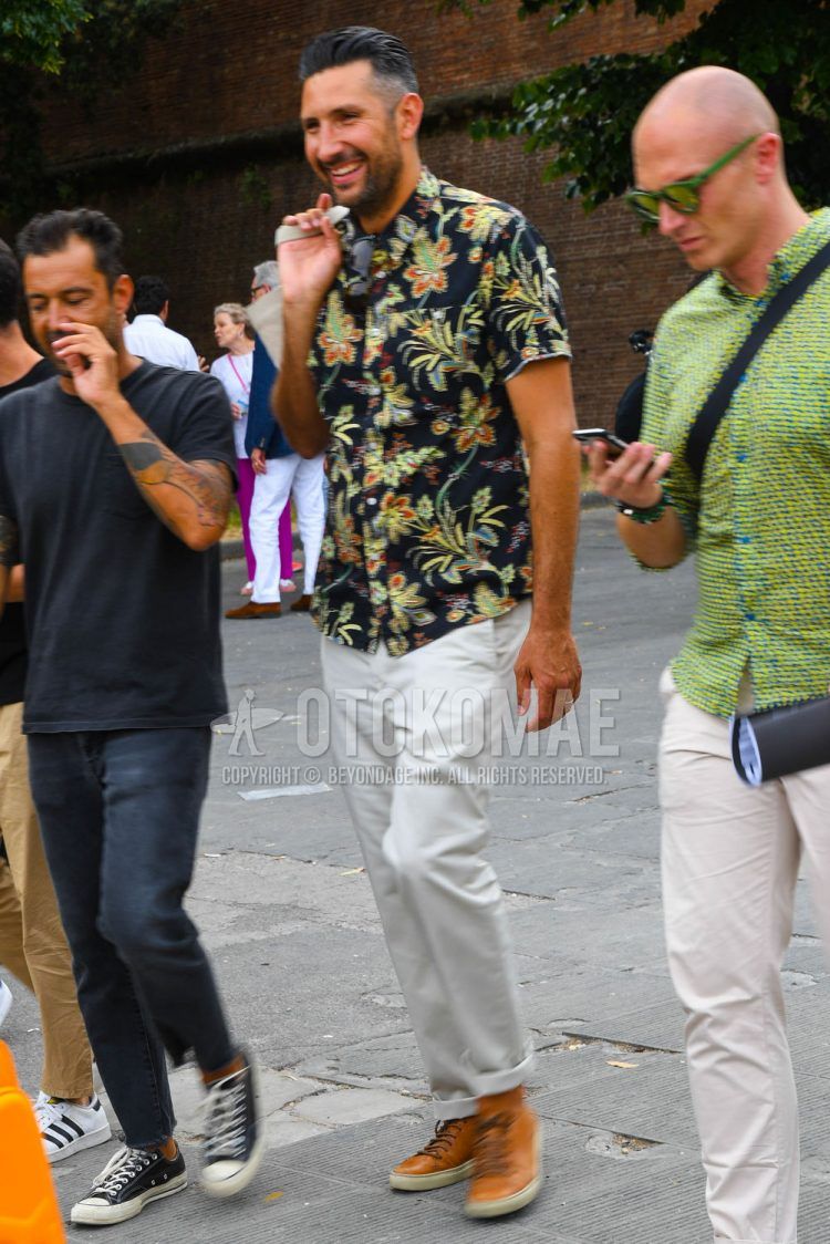 A spring/summer men's coordinate outfit with a black botanical shirt, plain white chinos, and brown high-cut sneakers.