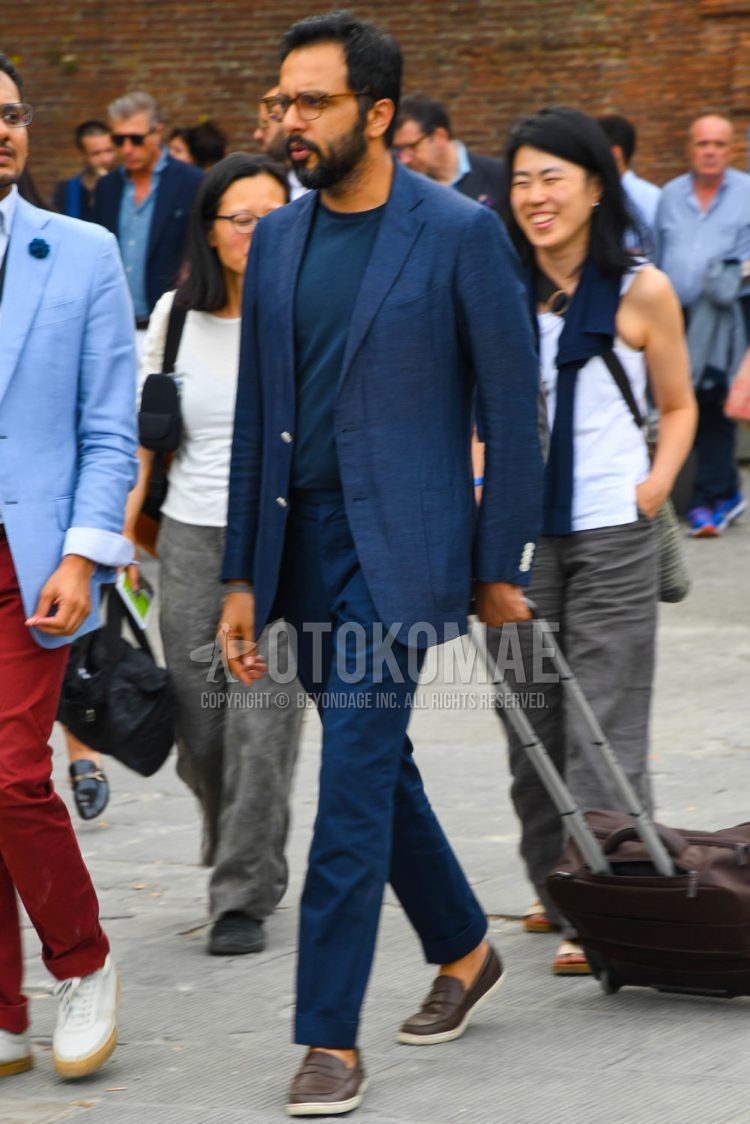 Spring, summer and fall men's coordinate outfit with tortoiseshell glasses, plain blue/navy t-shirt, brown slip-on sneakers, brown coin loafer leather shoes and plain navy suit.