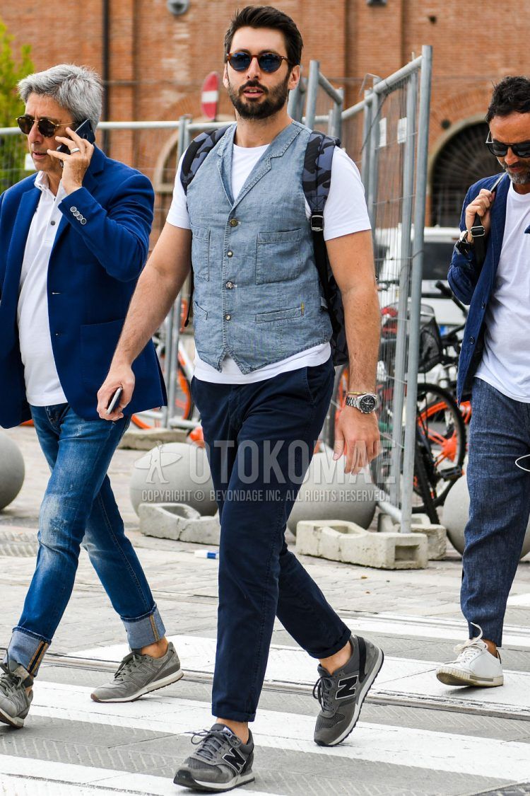 Spring, summer, and fall men's coordinate outfit with plain gray gilet, plain white T-shirt, plain navy chinos, and dark gray low-cut New Balance sneakers.