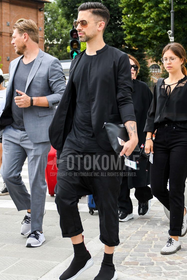 A men's spring/summer/fall outfit for men with solid color sunglasses, solid color black shirt, solid color black t-shirt, solid color black sarouel pants, solid color black slip-on sneakers, and solid color black Fendi clutch/second bag/drawstring bag.