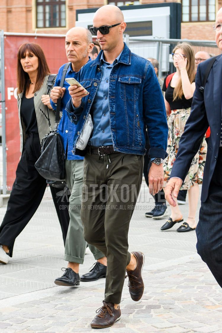 A spring/summer/fall men's coordinate outfit with solid color sunglasses, solid color navy denim jacket, solid color light blue shirt, solid color brown mesh belt, solid color olive green easy pants, and brown low-cut sneakers.
