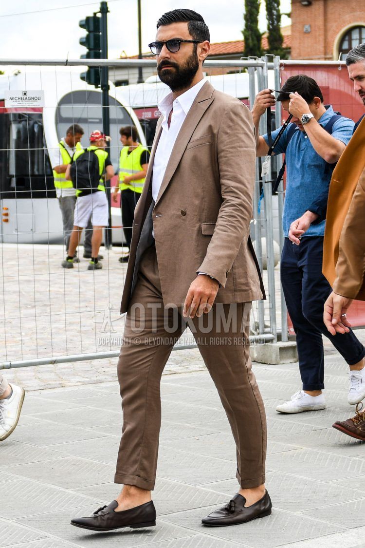 A men's spring, summer, and fall outfit of plain sunglasses, a plain white shirt, brown tassel loafer leather shoes, and a plain brown suit.
