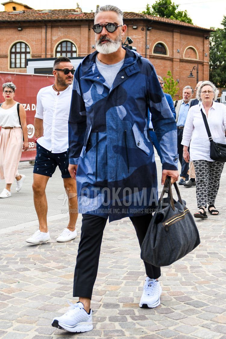 A men's spring/summer/fall outfit for men with plain black sunglasses, blue camouflage hooded coat, plain gray t-shirt, plain navy slacks, white low-cut sneakers, and plain white briefcase/handbag.