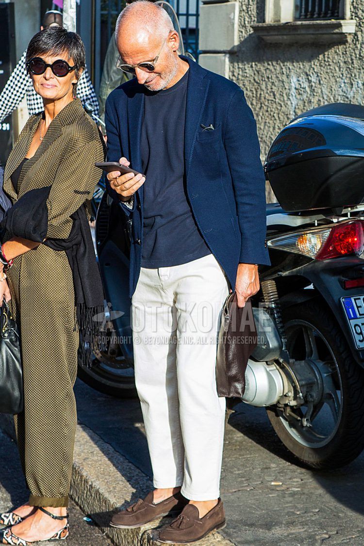 A spring/fall men's outfit with plain sunglasses, plain navy tailored jacket, plain navy t-shirt, plain white denim/jeans, brown tassel loafers leather shoes, brown suede shoes leather shoes, plain brown clutch bag/second bag/drawstring bag.