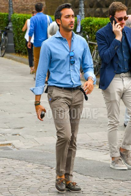 A spring/summer men's coordinate outfit with solid color sunglasses, solid color blue denim/chambray shirt, solid color mesh belt, solid color gray chinos, and gray moccasins/deck shoes leather shoes.