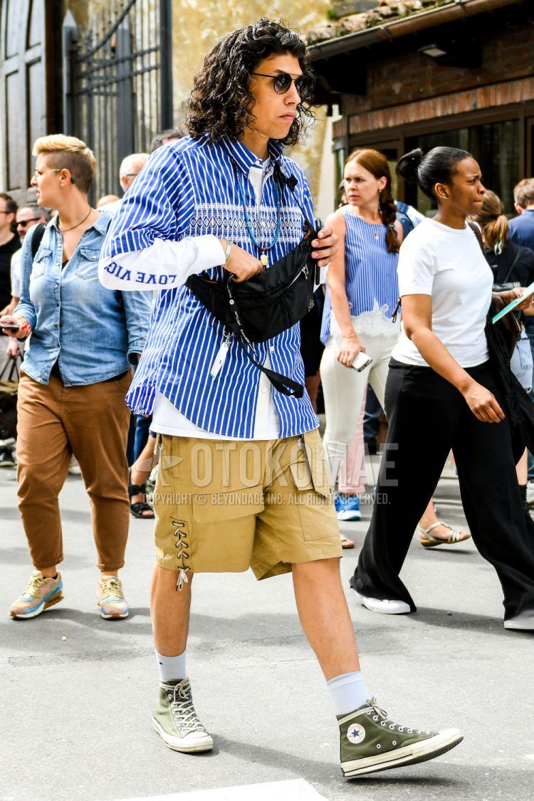 A summer men's coordinate outfit with plain sunglasses, blue striped shirt, white graphic t-shirt, plain beige cargo pants, plain white socks, Converse All Star olive green high-cut sneakers, and plain black sackosh.