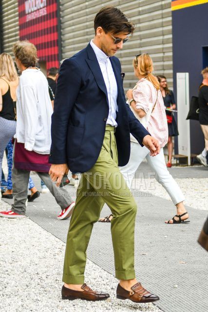 A summer-spring-fall menswear outfit with plain sunglasses, plain navy tailored jacket, plain white shirt, plain olive green beltless pants, plain slacks, brown monk shoes leather shoes, and other loafer leather shoes.
