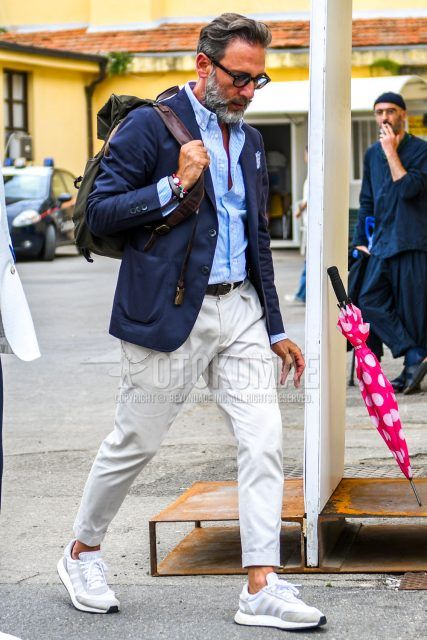 Spring, summer and fall men's coordinate outfit with brown tortoiseshell sunglasses, plain navy tailored jacket, light blue striped shirt, plain black mesh belt, plain white chinos, white low-cut sneakers and plain black backpack.