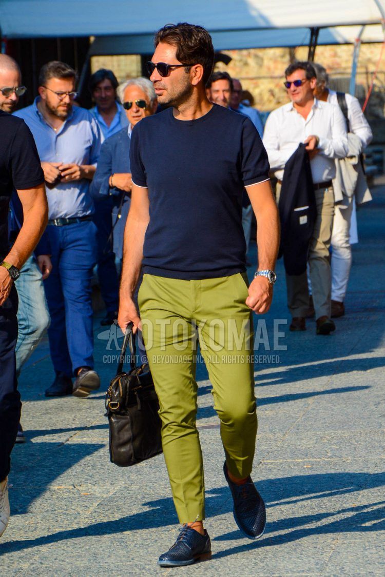 A spring/summer men's coordinate outfit with plain sunglasses, a plain navy t-shirt, plain olive green cotton pants, and navy low-cut sneakers.