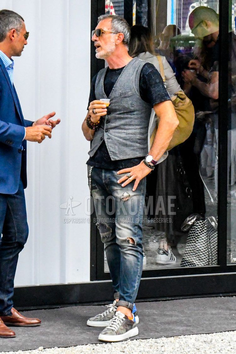 A spring/summer men's coordinate outfit with plain sunglasses, black other t-shirt, plain gray gilet, plain blue damaged jeans, and gray low-cut sneakers.