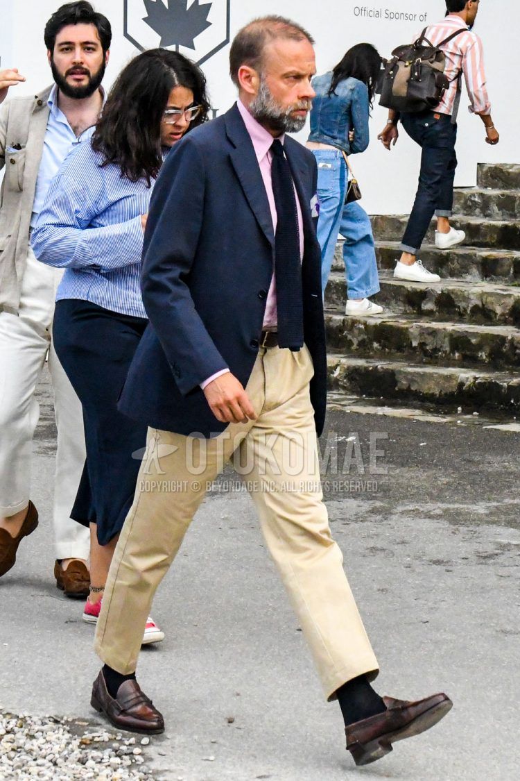 Spring, summer, and fall men's coordinate outfit with plain navy tailored jacket, plain pink shirt, plain brown leather belt, plain beige ankle pants, plain beige chinos, plain black socks, brown coin loafer leather shoes, and plain navy knit tie.