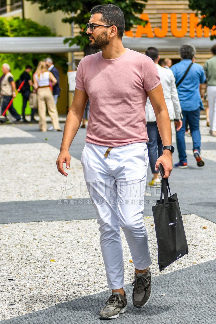 Men's spring/summer/fall outfit with plain black sunglasses, plain pink t-shirt, plain beige tape belt, plain white chinos, gray low-cut sneakers, and black lettered tote bag.