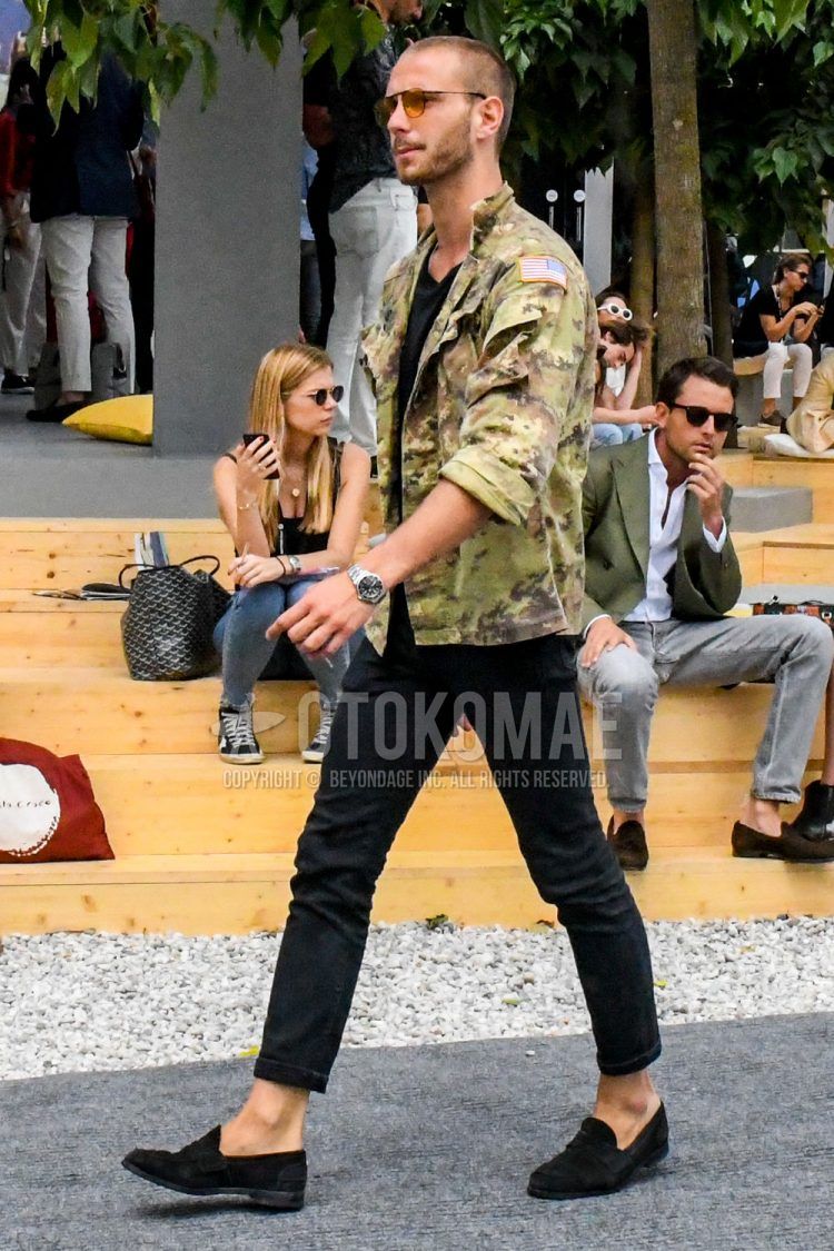 A summer/fall/spring men's coordinate outfit with solid color sunglasses, green camouflage shirt jacket, solid color black t-shirt, solid color black cropped pants, and suede black coin loafer leather shoes.