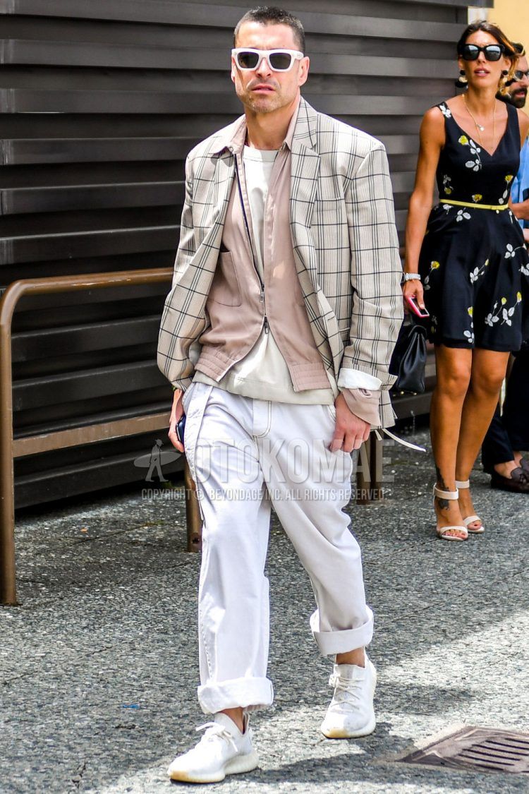 A men's spring/summer/fall outfit for men with solid color sunglasses, beige checked tailored jacket, solid color pink other, solid color beige t-shirt, solid color white wide pants, and white low-cut Adidas sneakers.