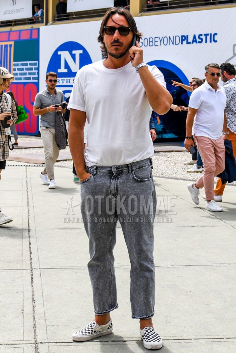 A summer men's coordinate outfit with solid color sunglasses, solid color white t-shirt, solid color gray ankle pants, solid color gray denim/jeans, and Vans white and black slip-on sneakers.