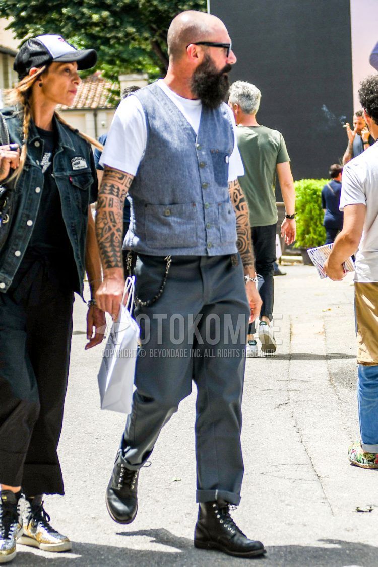 A spring/summer/fall men's coordinate outfit with plain black sunglasses, plain gray/blue gilet, plain white t-shirt, plain gray chinos, and black work boots.