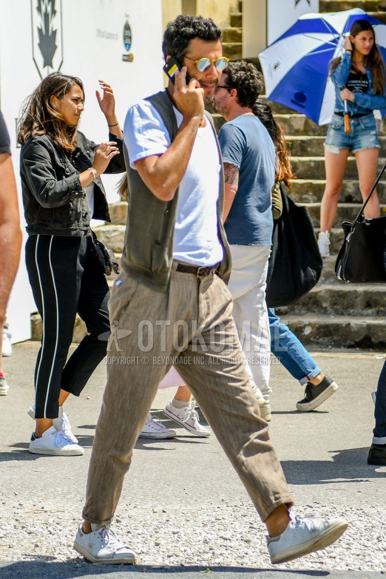 Summer men's coordinate outfit with tortoiseshell sunglasses, plain beige gilet, plain white t-shirt, plain brown mesh belt, plain leather belt, plain beige pleated pants, plain ankle pants, and Adidas Stan Smith white low-cut sneakers.