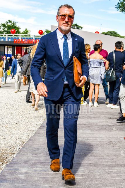 A men's spring/summer/fall outfit with solid color sunglasses, solid color white shirt, brown monk shoes leather shoes, brown wingtip leather shoes, solid color brown clutch bag/second bag/drawstring, solid color navy suit, and solid color blue knit tie.