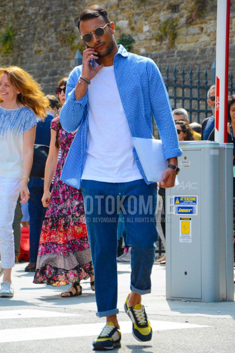 A spring/summer men's coordinate outfit with plain sunglasses, blue checked shirt, plain white t-shirt, plain blue denim/jeans, and yellow/black low-cut sneakers.