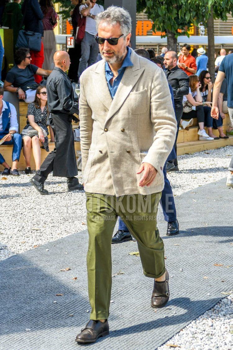 Spring, summer and fall men's coordinate outfit with solid color sunglasses, solid color beige tailored jacket, solid color blue denim/chambray shirt, solid color olive green cargo pants and olive green monk shoes leather shoes.