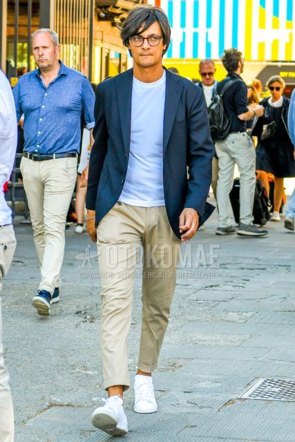 A men's fall/summer/spring outfit with plain glasses, plain navy tailored jacket, plain white t-shirt, plain beige chinos, and white low-cut sneakers.