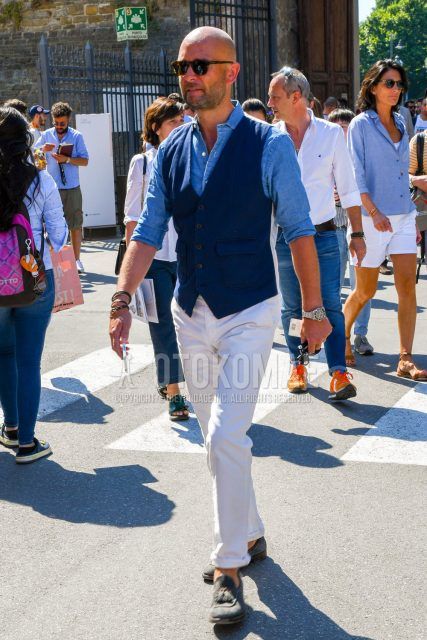 Men's spring/summer/fall outfit with solid color sunglasses, solid color navy gilet, solid color blue denim/chambray shirt, solid color white cropped pants, gray tassel loafers leather shoes, suede shoes leather shoes.