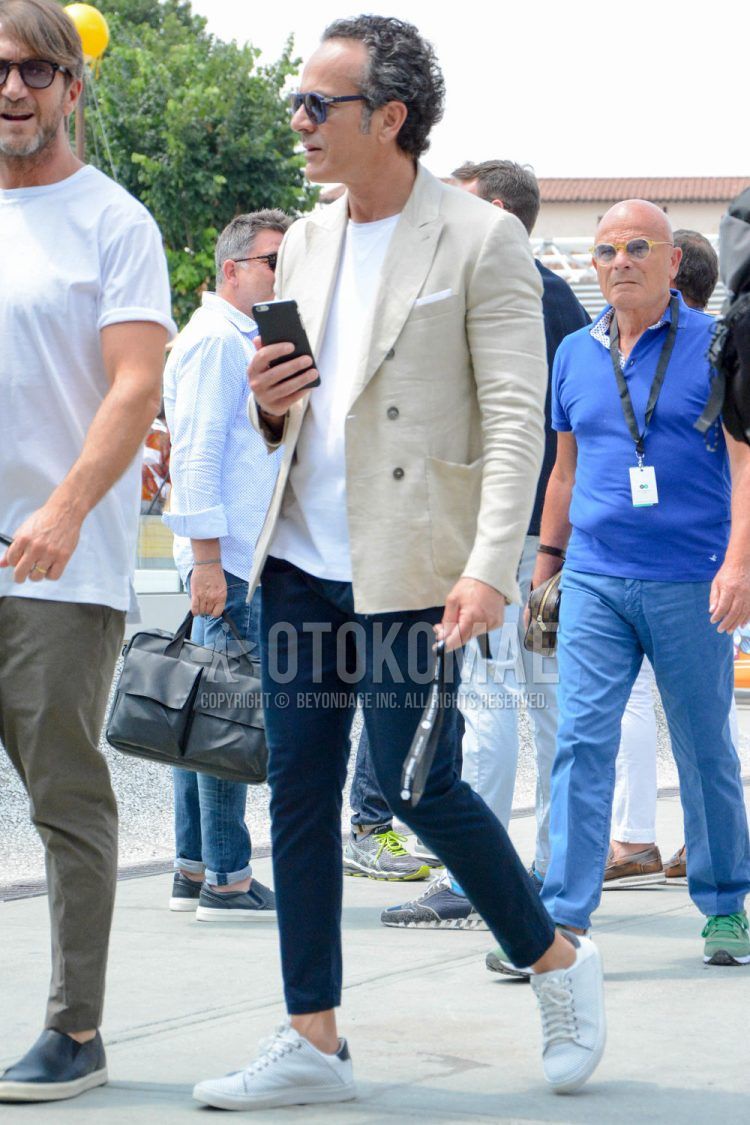 A men's spring/summer/fall coordinate outfit with plain sunglasses, a plain beige tailored jacket, a plain white T-shirt, plain navy chinos, and white low-cut sneakers.