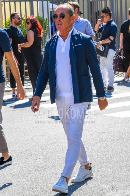A men's spring/summer/fall outfit with plain sunglasses, plain navy tailored jacket, plain white polo shirt, plain white slacks, and white low-cut sneakers by Golden Goose Starter.