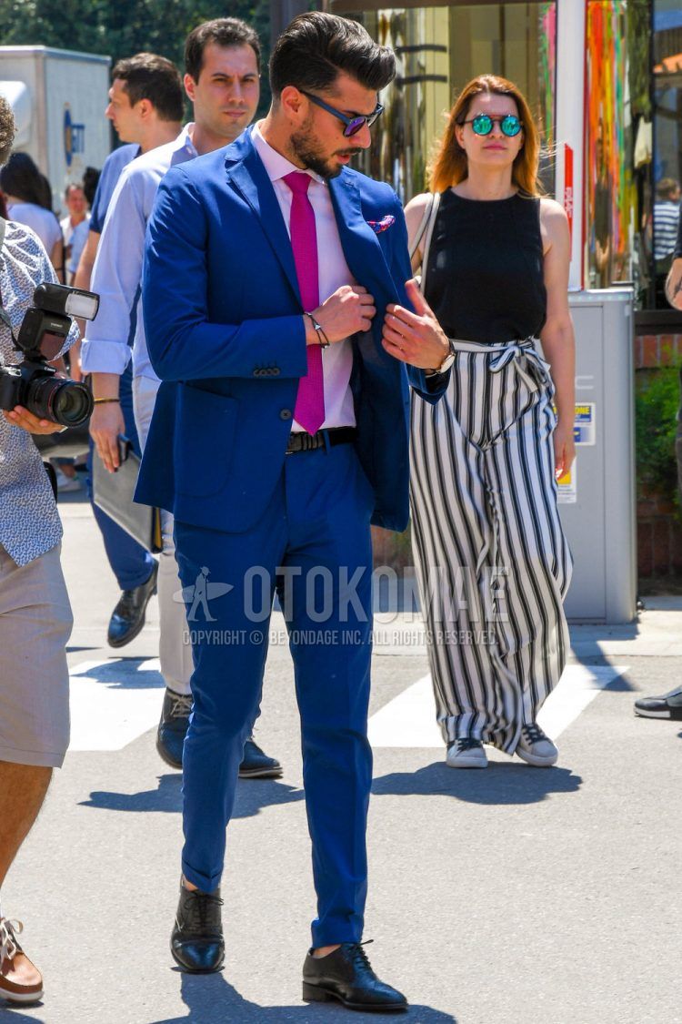 A men's spring, summer, and fall outfit with solid color sunglasses, solid color pink shirt, solid color black leather belt, black plain toe leather shoes, solid color blue suit, and solid color pink tie.