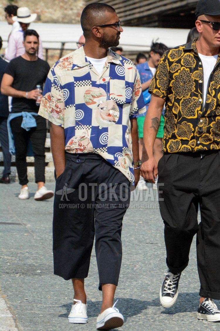 A spring/summer men's coordinate outfit with plain sunglasses, plain white t-shirt, multi-colored and other shirts, plain black chinos, and white low-cut sneakers.