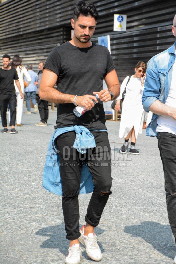 A men's spring/summer coordinate outfit with a plain black T-shirt, plain black damaged jeans, and white low-cut sneakers.