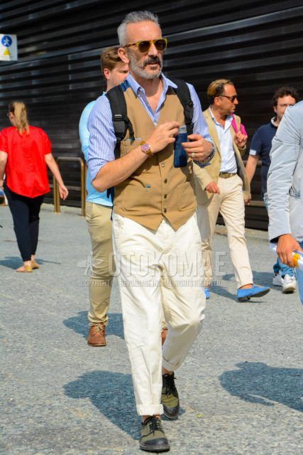 A spring/summer men's coordinate outfit with solid color sunglasses, solid color beige gilet, blue striped shirt, solid color beige cotton pants, and green low-cut sneakers.