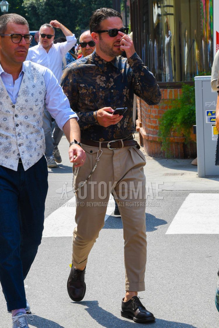 Summer/spring men's coordinate outfit with plain sunglasses, brown botanical shirt, plain brown leather belt, plain beige chinos, and black/brown plain-toe leather shoes.