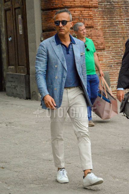 A men's spring/summer/fall outfit for men with plain sunglasses, a plain blue tailored jacket, a plain blue polo shirt, plain white cotton pants, and white low-cut sneakers.