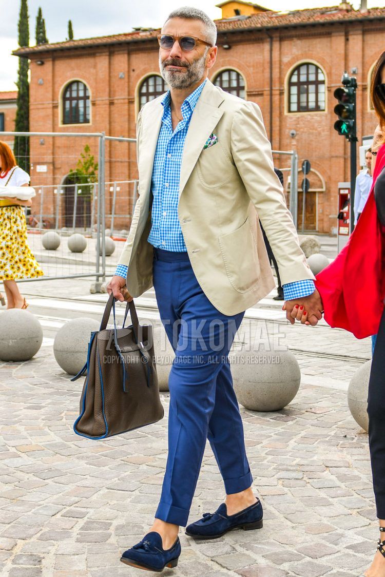 Men's spring/summer/fall outfit with plain brown sunglasses, plain beige tailored jacket, light blue/white checked shirt, plain blue slacks, navy tassel loafer leather shoes, and plain brown/light blue tote bag.