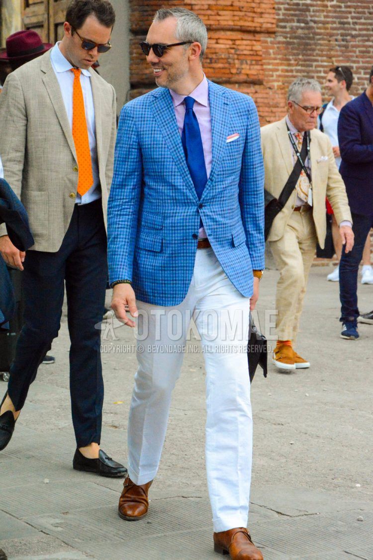 Men's spring/summer/fall outfit with solid color sunglasses, blue checked tailored jacket, solid color pink shirt, solid color brown leather belt, solid color white slacks, brown monk shoe leather shoes, and solid color navy tie.