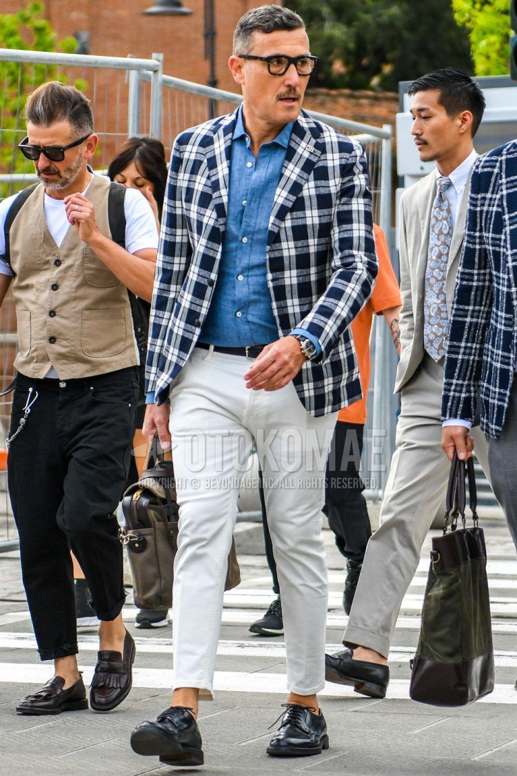 A summer/fall/spring men's outfit with solid color glasses, white/navy check tailored jacket, solid color blue denim/chambray shirt, solid color black leather belt, solid color white ankle pants, black plain toe leather shoes, and solid color olive green briefcase/handbag.