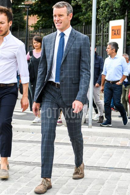 Spring, summer and fall men's coordinate outfit with white dotted shirt, plain brown leather belt, brown brogue shoes leather shoes, dark gray check suit and plain blue knit tie.