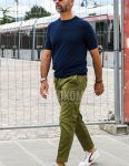 A spring/summer men's coordinate outfit with solid color sunglasses, solid color navy sweater, solid color olive green cotton pants, and white low-cut sneakers.