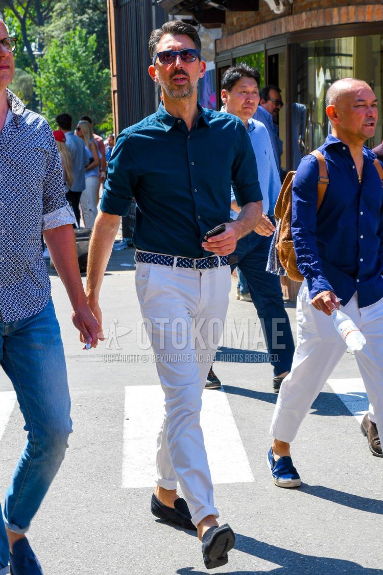 Spring, summer and fall men's coordinate outfit with solid color sunglasses, solid color navy shirt, solid color navy mesh belt, solid color white slacks and navy moccasin/deck shoes leather shoes.