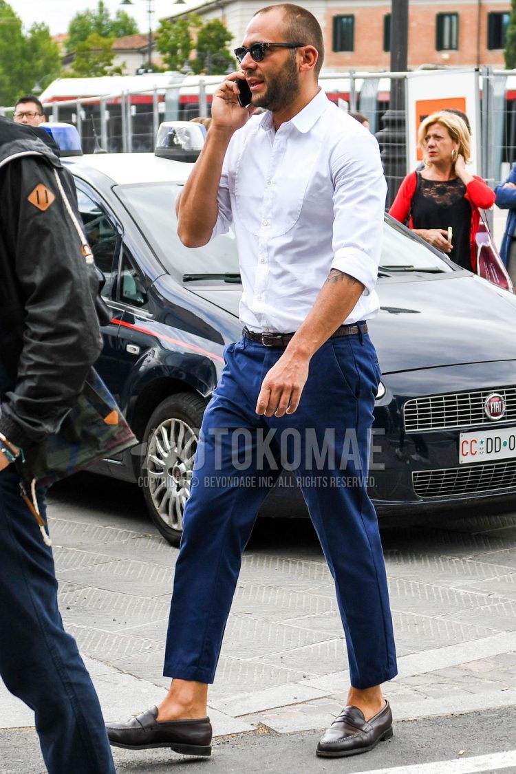 Men's spring, summer, and fall men's coordinate outfit with solid color sunglasses, solid color white shirt, solid color brown leather belt, solid color navy ankle pants, solid color navy cotton pants, and brown coin loafer leather shoes.