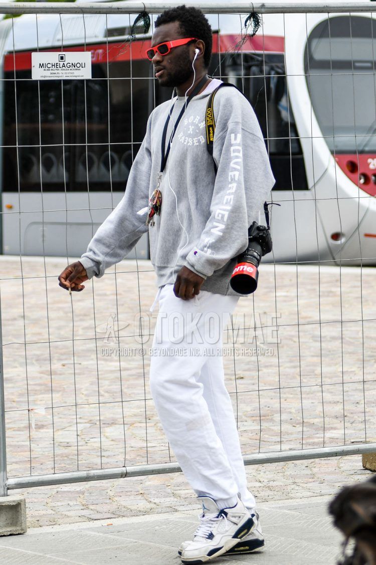 A spring/summer/fall men's coordinate outfit with plain sunglasses, gray graphic sweatshirt, plain white easy pants, plain white jogger pants/ribbed pants, and white low-cut Nike sneakers.