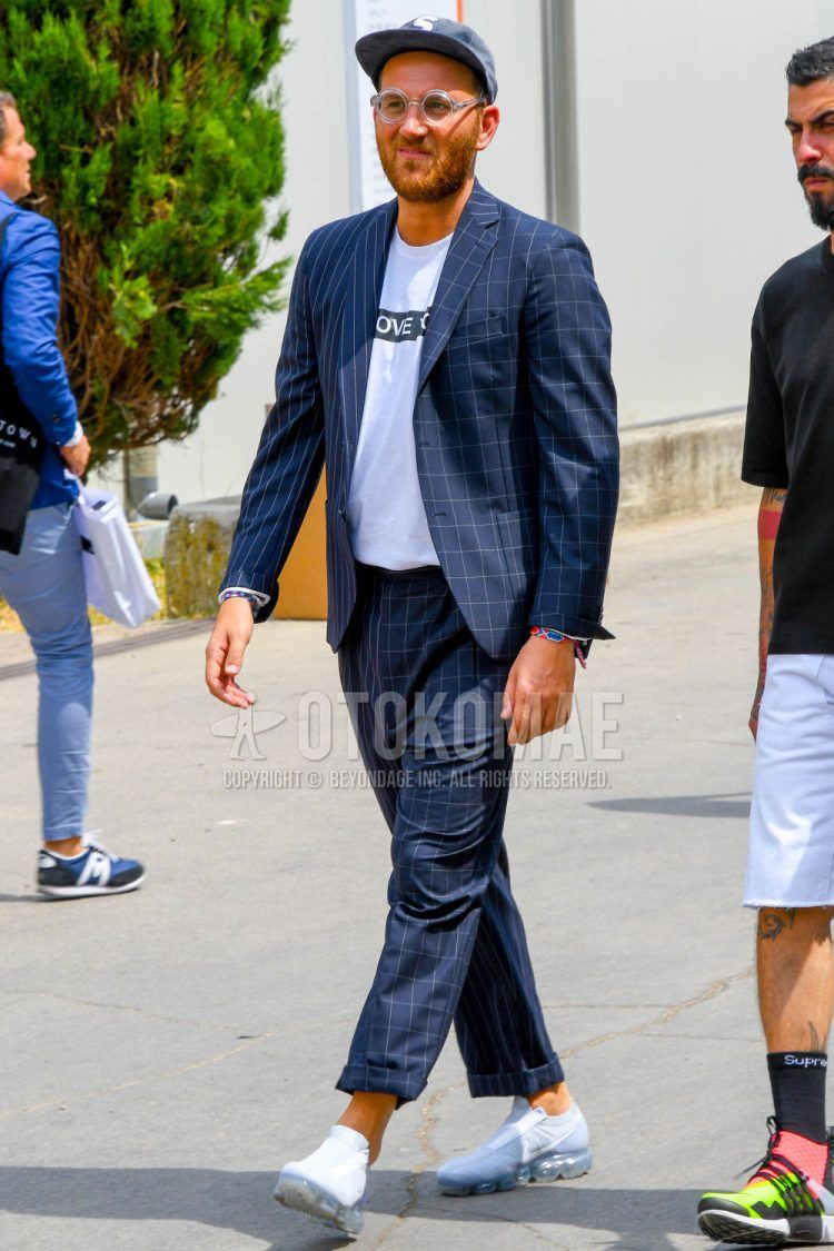 Spring, summer and fall men's coordinate outfit with plain baseball cap, plain glasses, white lettered t-shirt, white low-cut Nike sneakers and navy check suit.